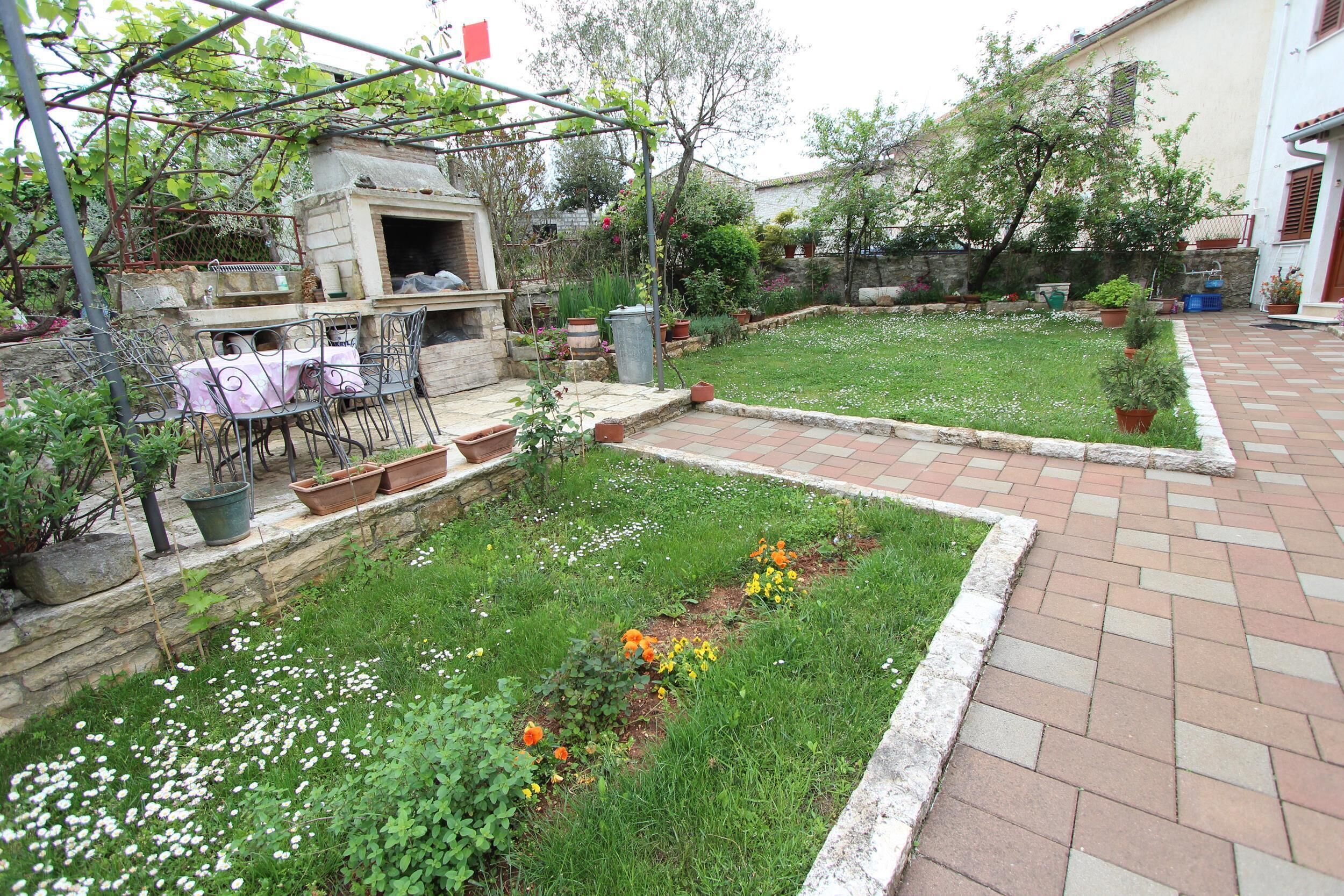 A courtyard with a brick pathway, a small garden with flowers, and a metal table with chairs.