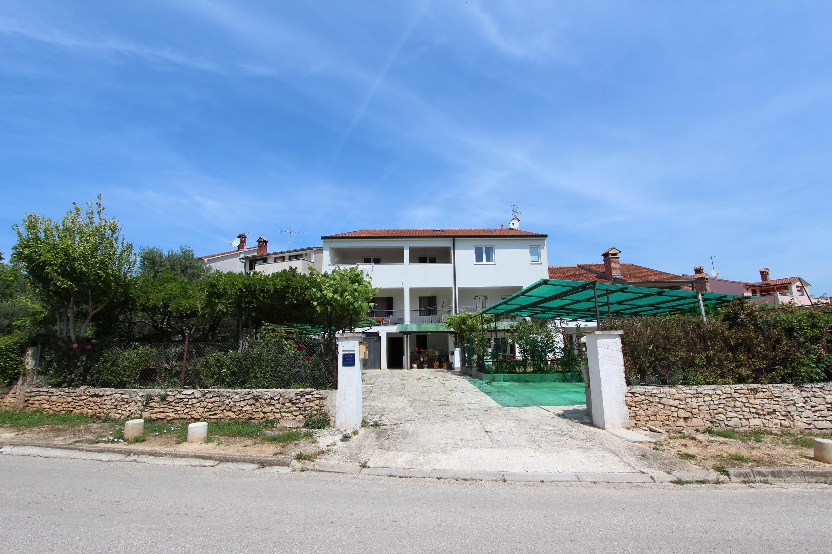 Un edificio a due piani con tetto in tegole rosse, un ingresso coperto e un muro in pietra di fronte.