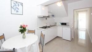 A compact kitchen with white cabinetry, a gas stove, a microwave, and a sink. There is a dining table with chairs and a vase of flowers. - PALAZIOL Two-Bedroom Apartment 2 (Rovinj)