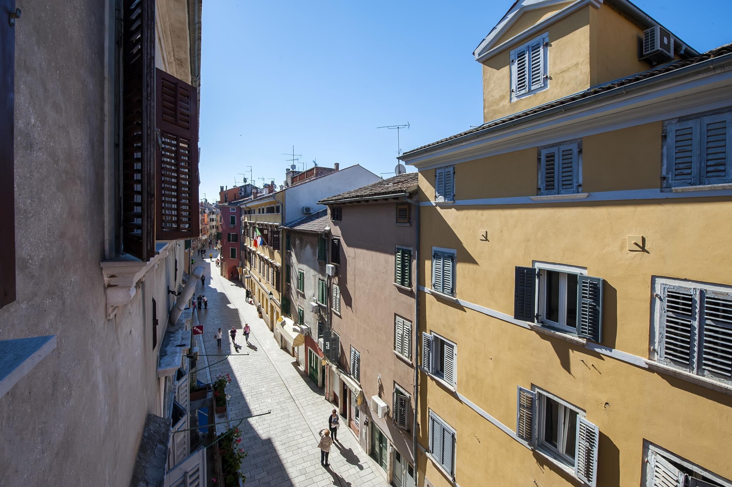A narrow street lined with traditional buildings, featuring balconies and shutters.