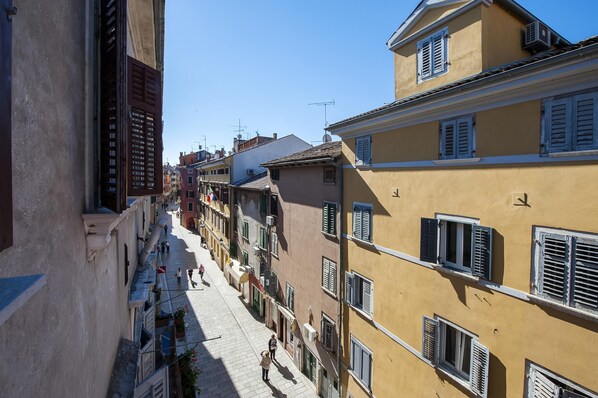 A narrow street lined with traditional buildings, featuring balconies and shutters.