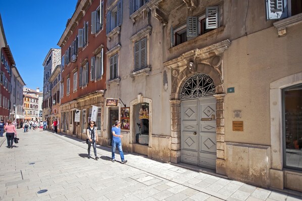 A pedestrian street with historic buildings, a shop with a signboard, and a person walking. - BAROCCO One-Bedroom Apartment (Rovinj)