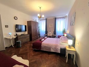 Et soveværelse med seng, kommode, fjernsyn, skrivebord, stol og et lille bord med lampe.