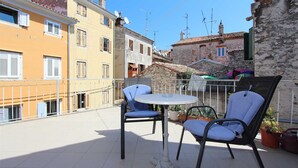 A balcony with a round table and two chairs, overlooking a street with buildings. - BAROCCO One-Bedroom Apartment (Rovinj)