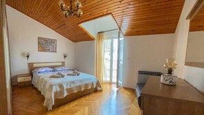 Une chambre avec un plafond en bois, un lit recouvert d’une courtepointe blanche, un radiateur et une fenêtre avec des rideaux.