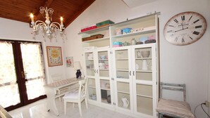 A room with a white table, chairs, a chandelier, a clock, and a storage unit with mesh doors. - APOLLONIO Studio Apartment with Terrace (Rovinj)