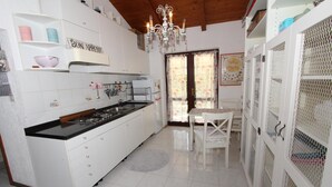 A kitchen with white cabinets, a gas stove, a sink, and a chandelier. There is a table with chairs and a window with floral curtains. - APOLLONIO Studio Apartment with Terrace (Rovinj)
