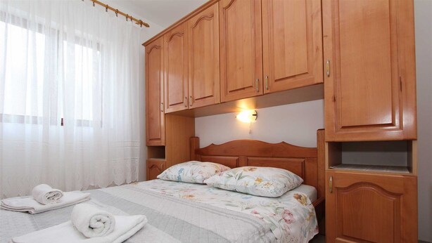 A bedroom with a bed, wooden cabinets, a nightstand, and a wall-mounted light. - MARUCHITA Two-Bedroom Apartment (Vesna, 1.kat) (Rovinj)