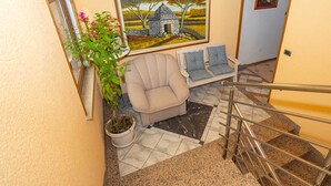 A staircase with a handrail, a beige armchair, a blue sofa, a potted plant, and a painting of a stone house. - VILLA FJORD Two-Bedroom Apartment 4 (Kanfanar)