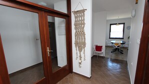 A modern interior with a wooden door, a macrame wall hanging, a dining area with a table and chairs, and a clock on the wall. - MITTON 2 Two-Bedroom Apartment (Motovunska) (Rovinj)