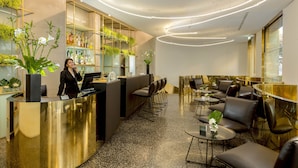 A modern reception area with a receptionist, a counter, seating area, and a bar. - Hotel Royal Bissolati (Rome)