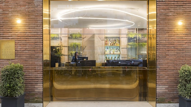 A hotel entrance with a glass facade, a reception desk, and a bar area visible through the glass. - Hotel Royal Bissolati (Rome)