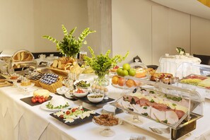 Monipuolinen buffet, jossa on tarjolla erilaisia ruokia ja koristeellinen kasvi.