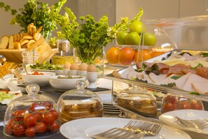 A buffet with various food items including bread, eggs, tomatoes, and meats.