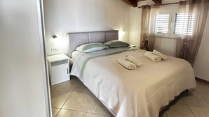 Ein Schlafzimmer mit Holzbalkendecke, einem Bett mit weißer Bettdecke, zwei Nachttischen und einem Fenster mit Vorhängen.
