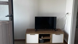 Ein Zimmer mit Fernseher auf einem Holzschrank, einer Tür und zwei an der Wand hängenden Bildern.