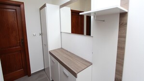 Una stanza piccola con una porta in legno, un mobiletto bianco e un ripiano.