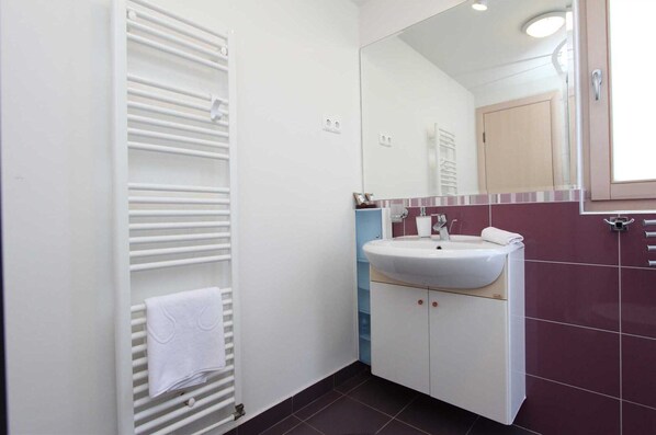 Un baño con un radiador blanco, un lavamanos con espejo y una toalla colgada del radiador.
