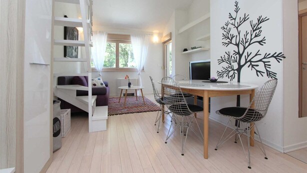 Un espacio moderno para vivir con comedor, sofá, televisor y un mural decorativo con un árbol.