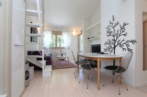 Un espacio moderno para vivir con comedor, sofá, televisor y un mural decorativo con un árbol.