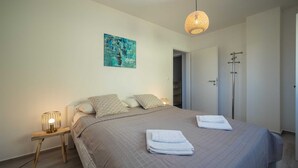 Een slaapkamer met een bed, nachtkastjes, een hanglamp, een deur en een schilderij aan de muur.
