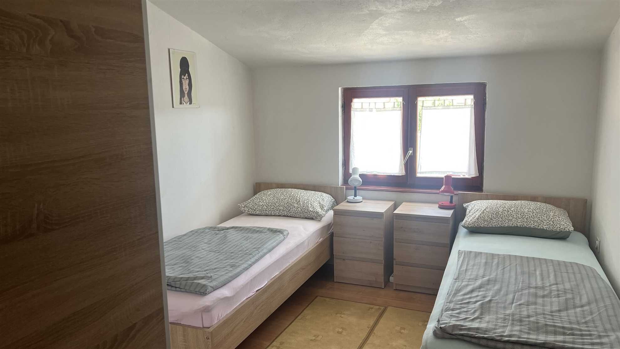 A small, single-room accommodation with two beds, a desk, and a window.
