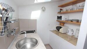 Een functionele keuken met een spoelbak, magnetron, waterkoker en planken met servies en glazen.