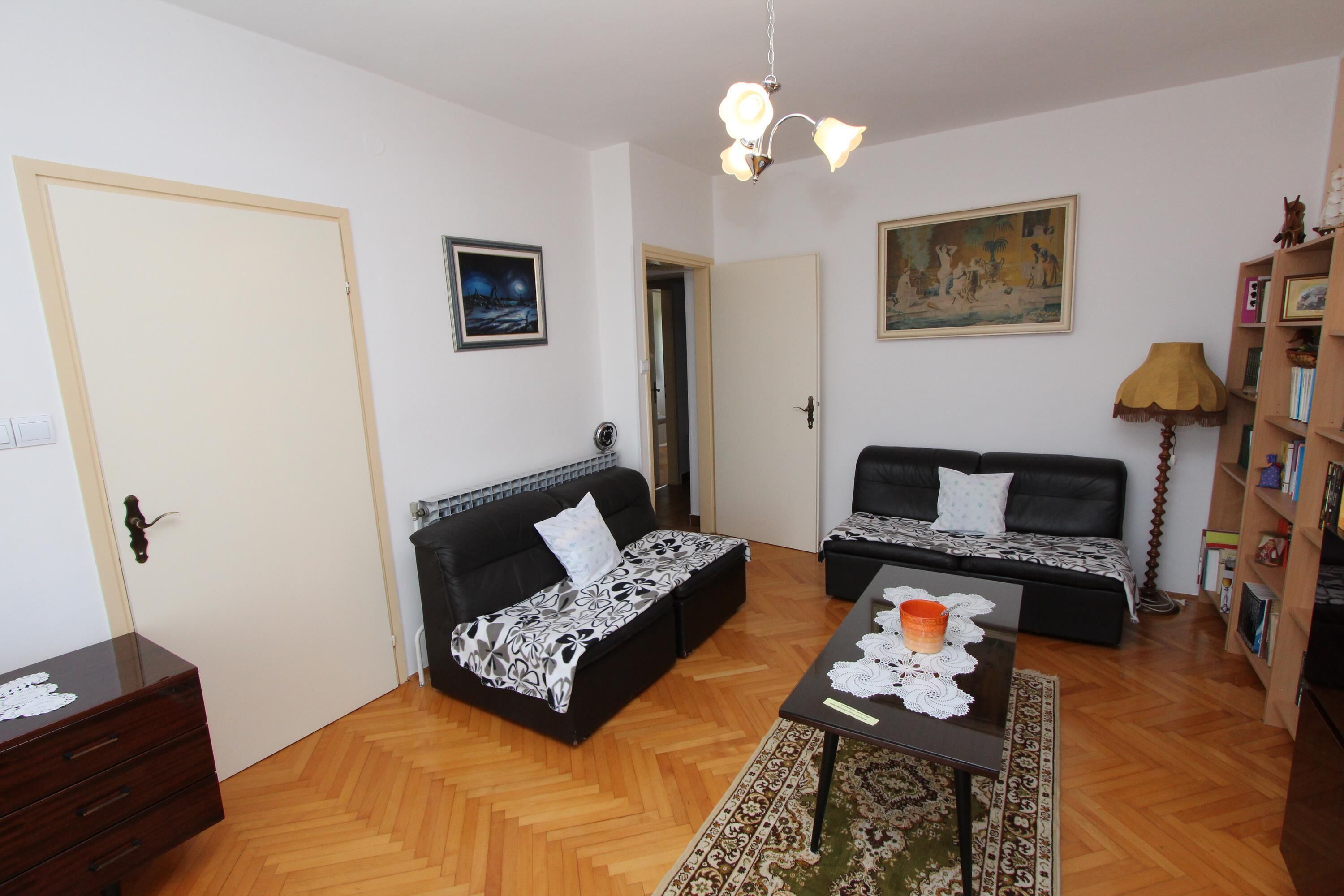 Ein Wohnzimmer mit zwei schwarzen Sofas, einem Holztisch, einem gemusterten Teppich, einem Bücherregal und einem Bild an der Wand.