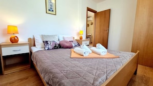Un lit bien fait, recouvert d’une courtepointe, deux tables de chevet avec des lampes, une armoire en bois et un tableau encadré accroché au mur.