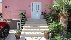 Un bâtiment à la façade rose, avec une porte blanche et un escalier menant à l’entrée.