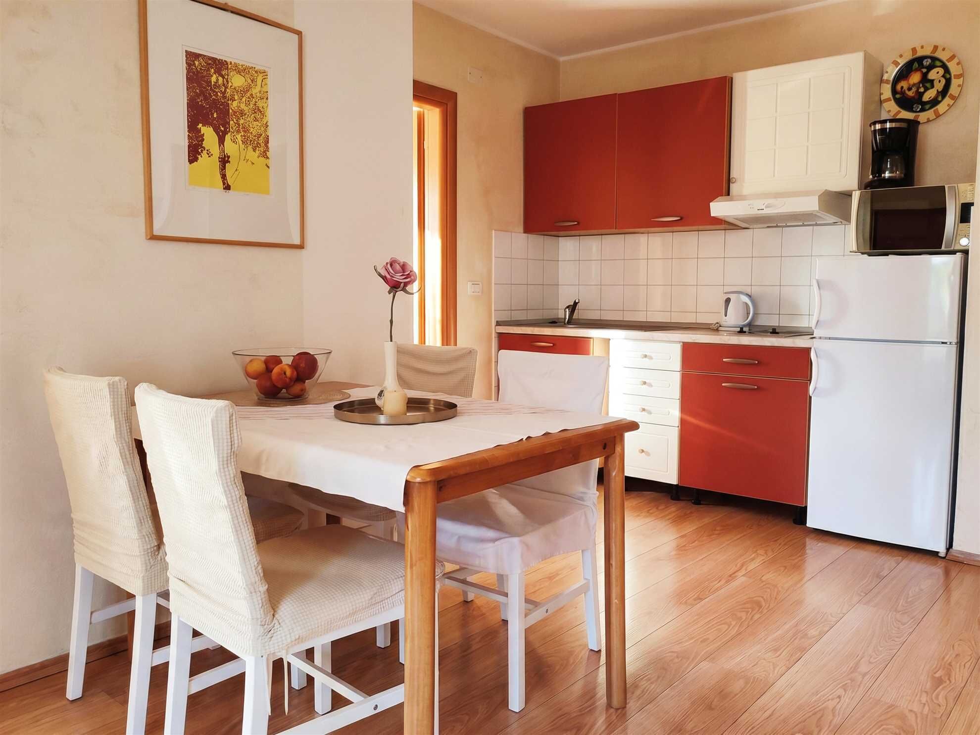 A dining area with a table, chairs, a vase with a flower, and a fruit bowl.