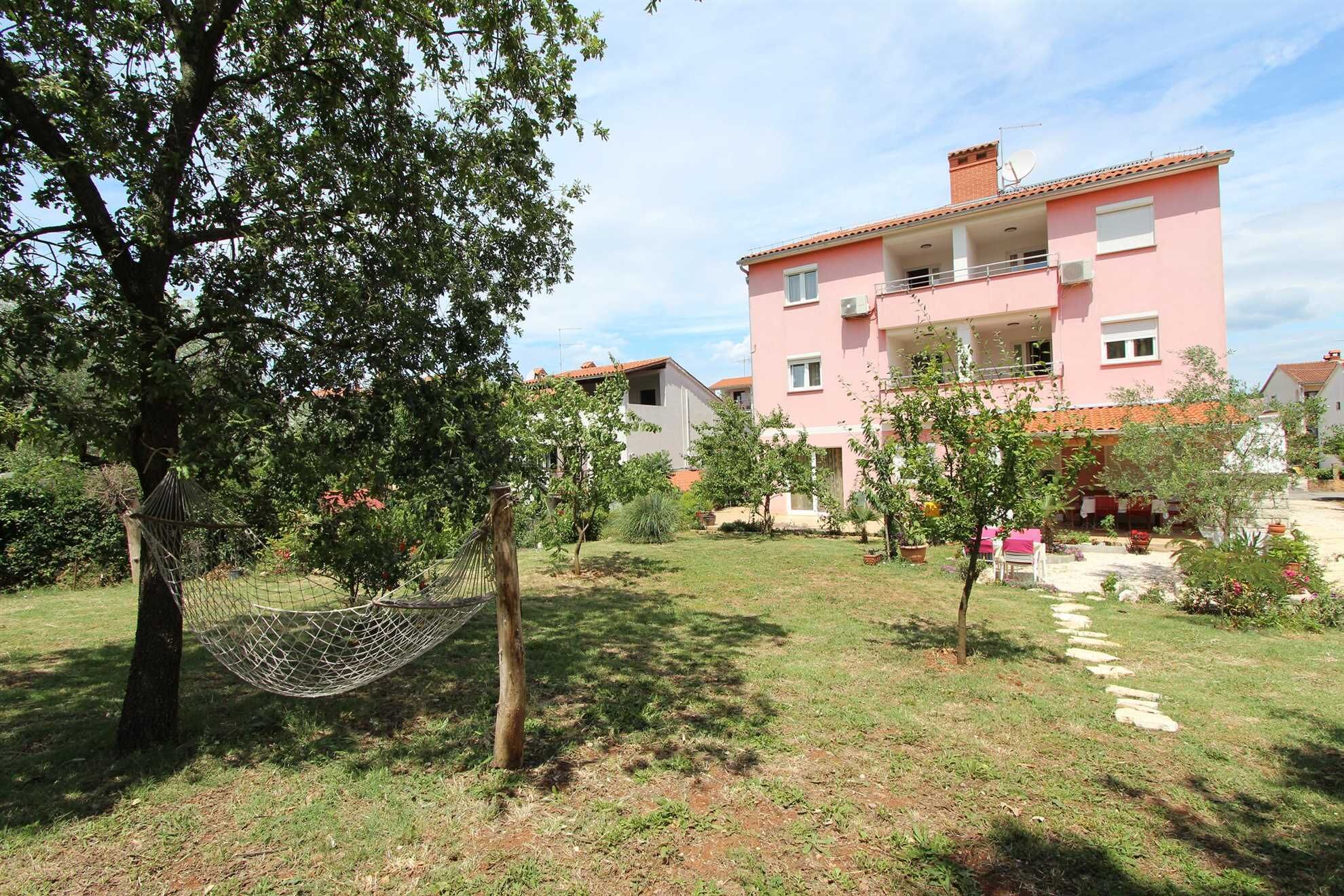 A pink building with a garden, a hammock, and a clear sky.