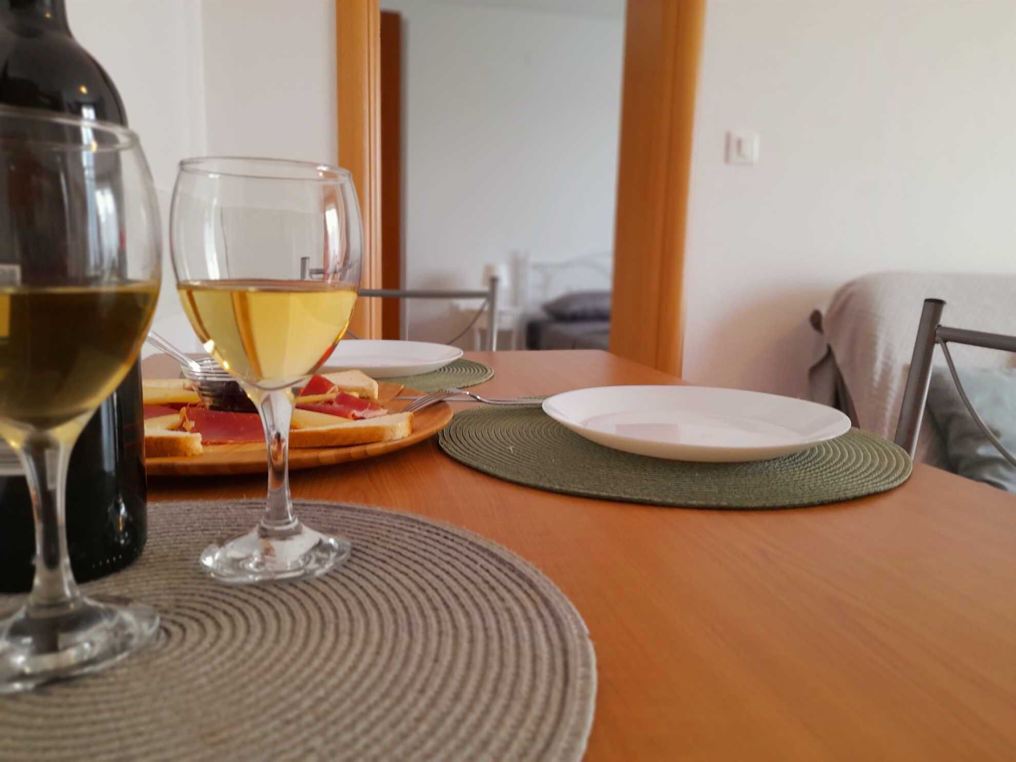 Een eettafel met een fles wijn, twee wijnglazen en een bord eten.