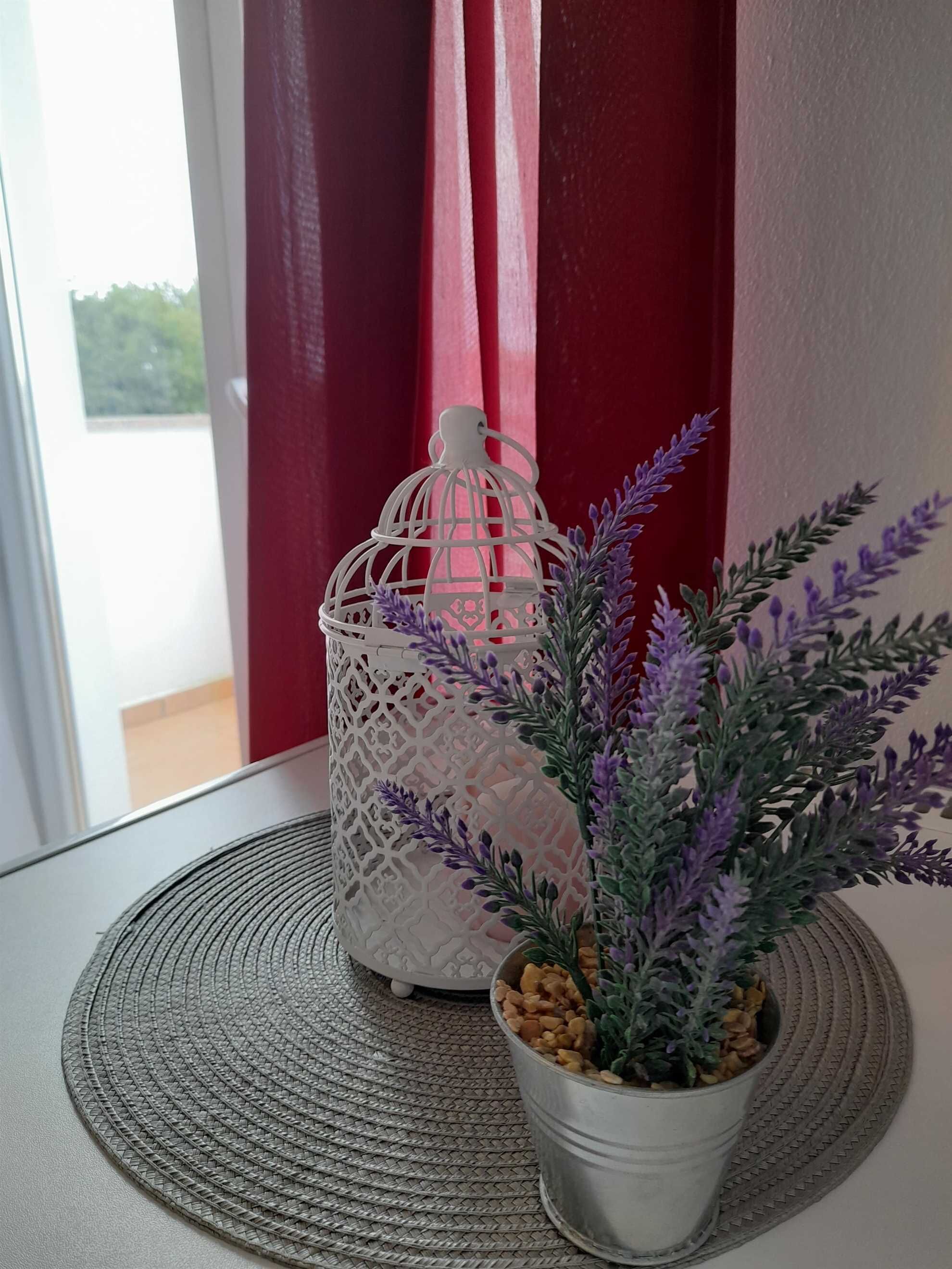 Een potplant met paarse bloemen op een geribbelde mat, naast een witte decoratieve lantaarn.