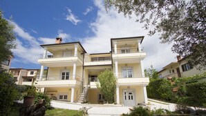A two-story building with a balcony, a staircase, and a small garden area with flowers and a tree. - RAJCI One-Bedroom Apartment 2 (plavi) (Rovinj)
