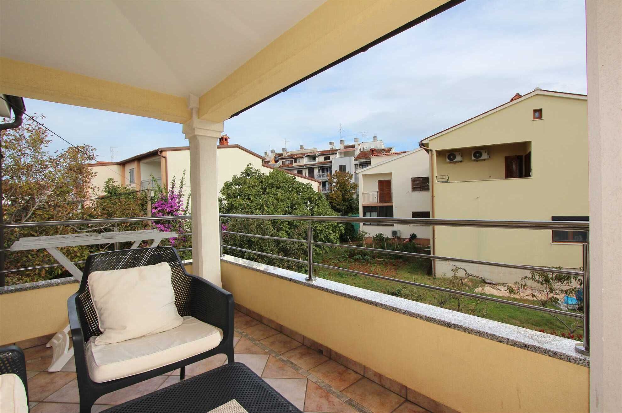 A balcony with a chair and table, overlooking a residential area with houses and greenery.