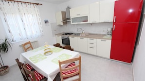 Zona de menjador amb taula preparada per a quatre persones, cuina amb armaris blancs i un frigorífic vermell, i finestra amb cortines.