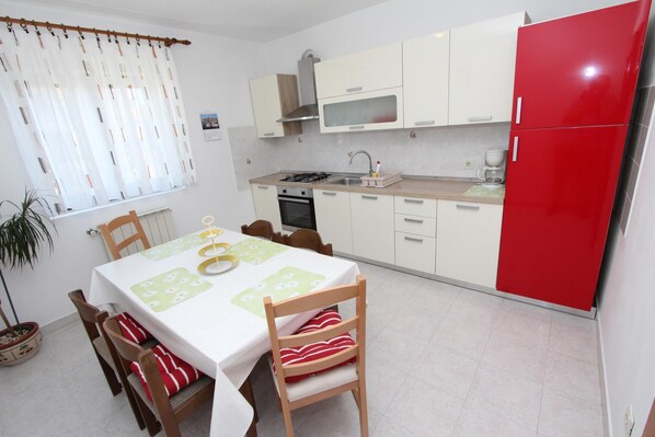 A dining area with a table set for four, a kitchen with white cabinets and a red refrigerator, and a window with curtains.