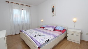 Un dormitori amb un llit, taules de nit, una lampaderia i una finestra amb cortines, i un llum fixat a la paret.