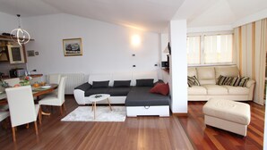 Un saló modern amb un sofà, una taula de dinar amb cadires, una taula blanca petita i una finestra amb cortines.