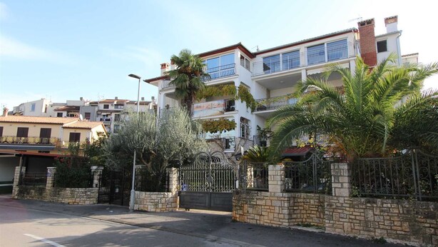 Un edifici residencial de diverses plantes amb balcons, parets de pedra i una entrada tancada.