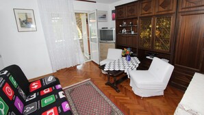 Ein Wohnzimmer mit einer Couch, einem weißen Sessel, einem Holzschrank, einem Fernseher und einem Tisch mit Blumenvase.