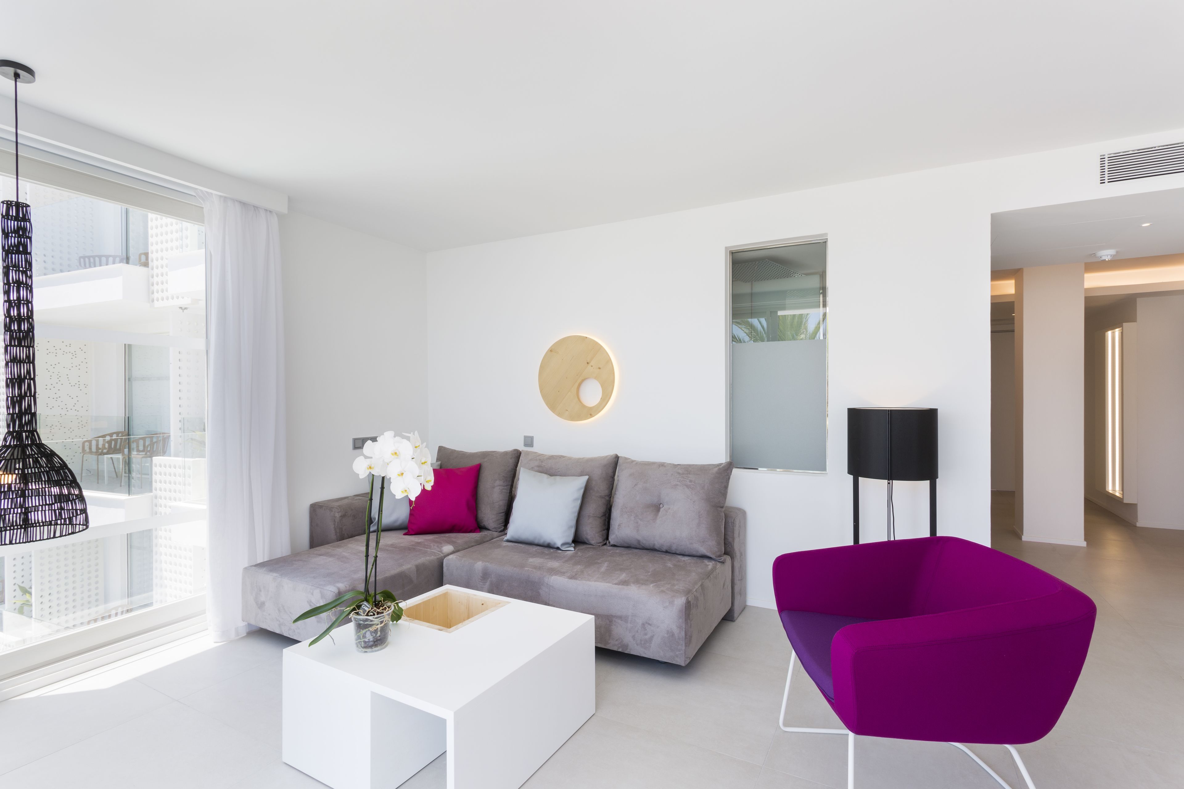 A modern living room with a grey sofa, white coffee table, and a purple armchair.