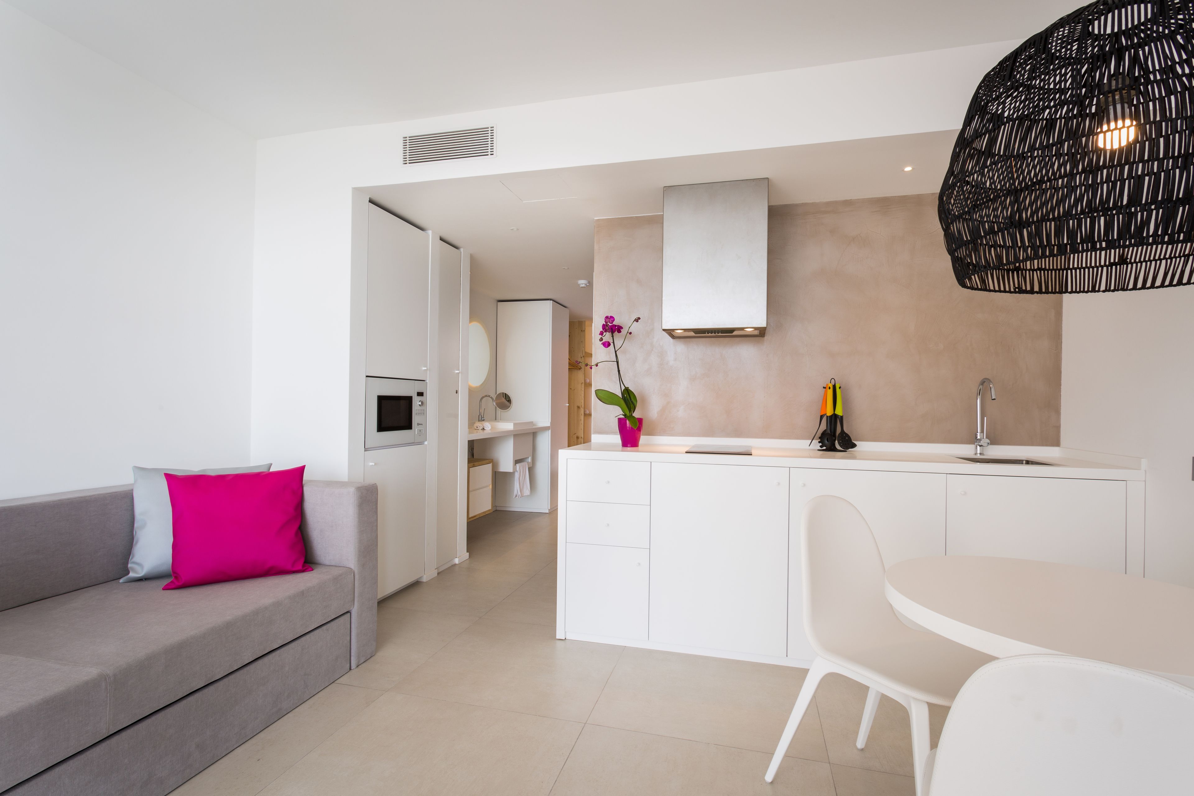 A modern kitchen with white cabinetry, a built-in oven, and a black hanging light fixture.