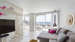 A modern living room with a large TV, a sofa with cushions, a coffee table, and a view of the beach through large windows. - One Ibiza Suites (Ibiza Town)