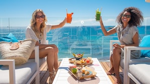 Two people toasting with drinks on a balcony overlooking a pool and ocean view. - One Ibiza Suites (Ibiza Town)