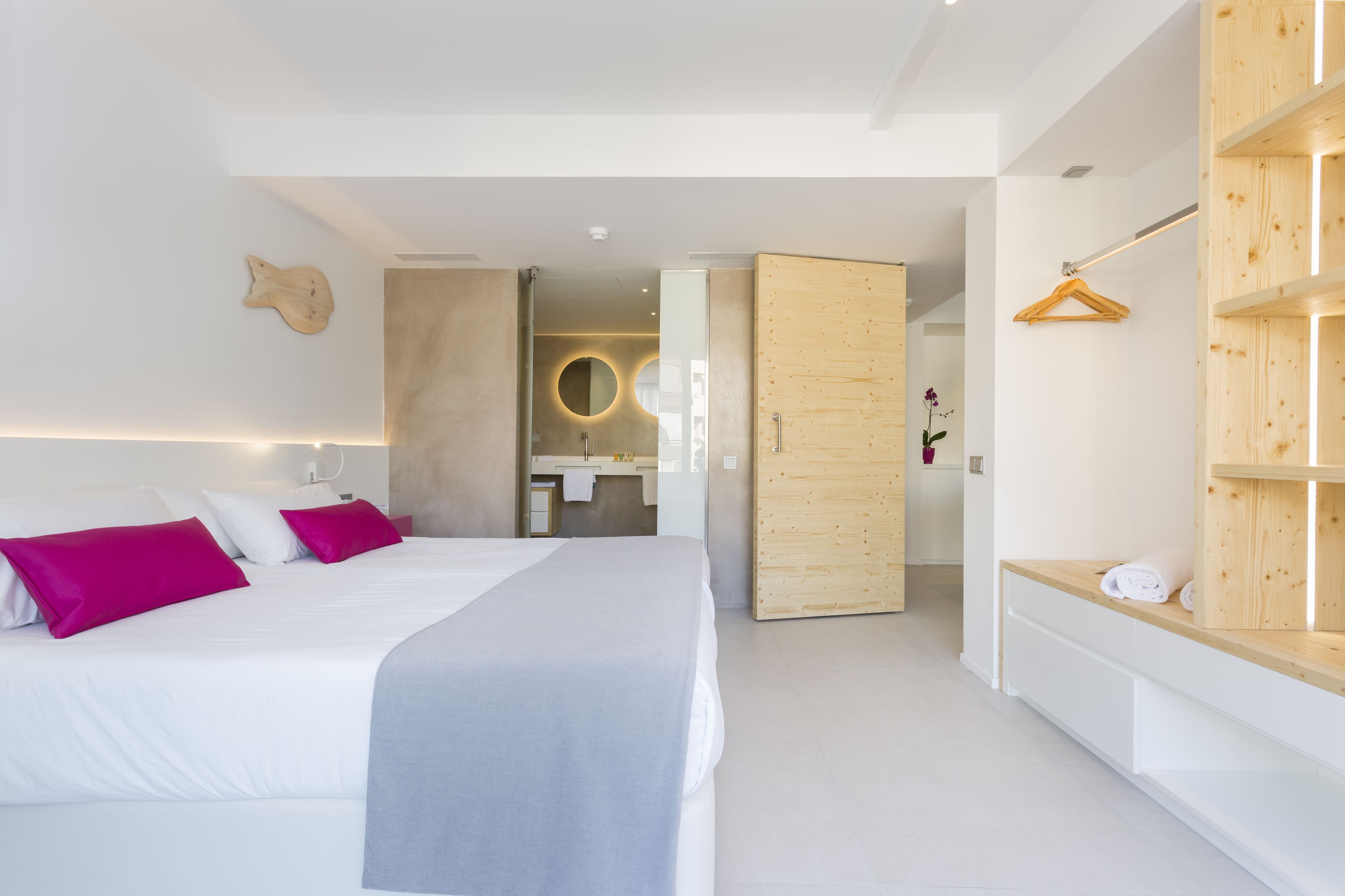 A modern bedroom with a large bed, a wooden wardrobe, and a bathroom visible through an open door.
