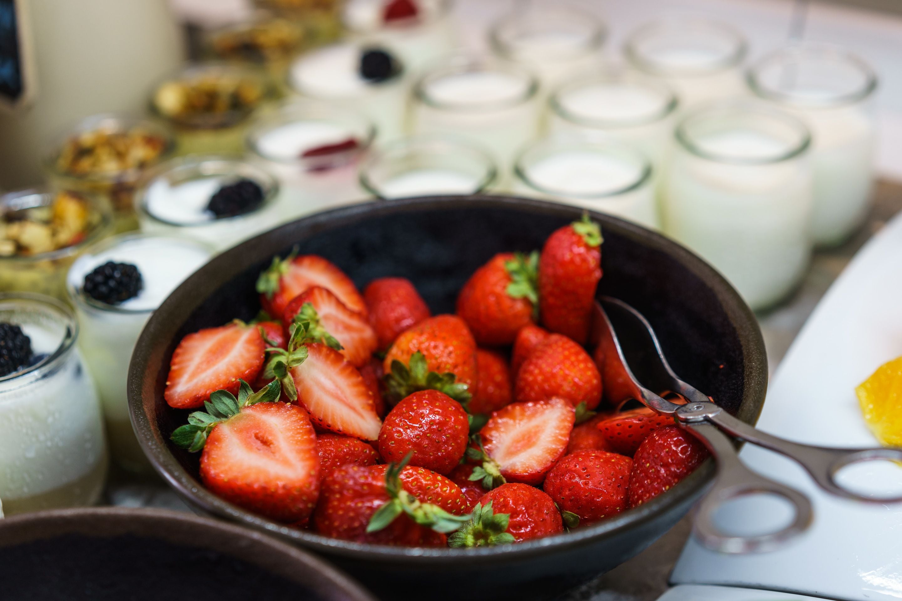 Un bol de fresas frescas con una cuchara, rodeado de diversos productos lácteos y postres.