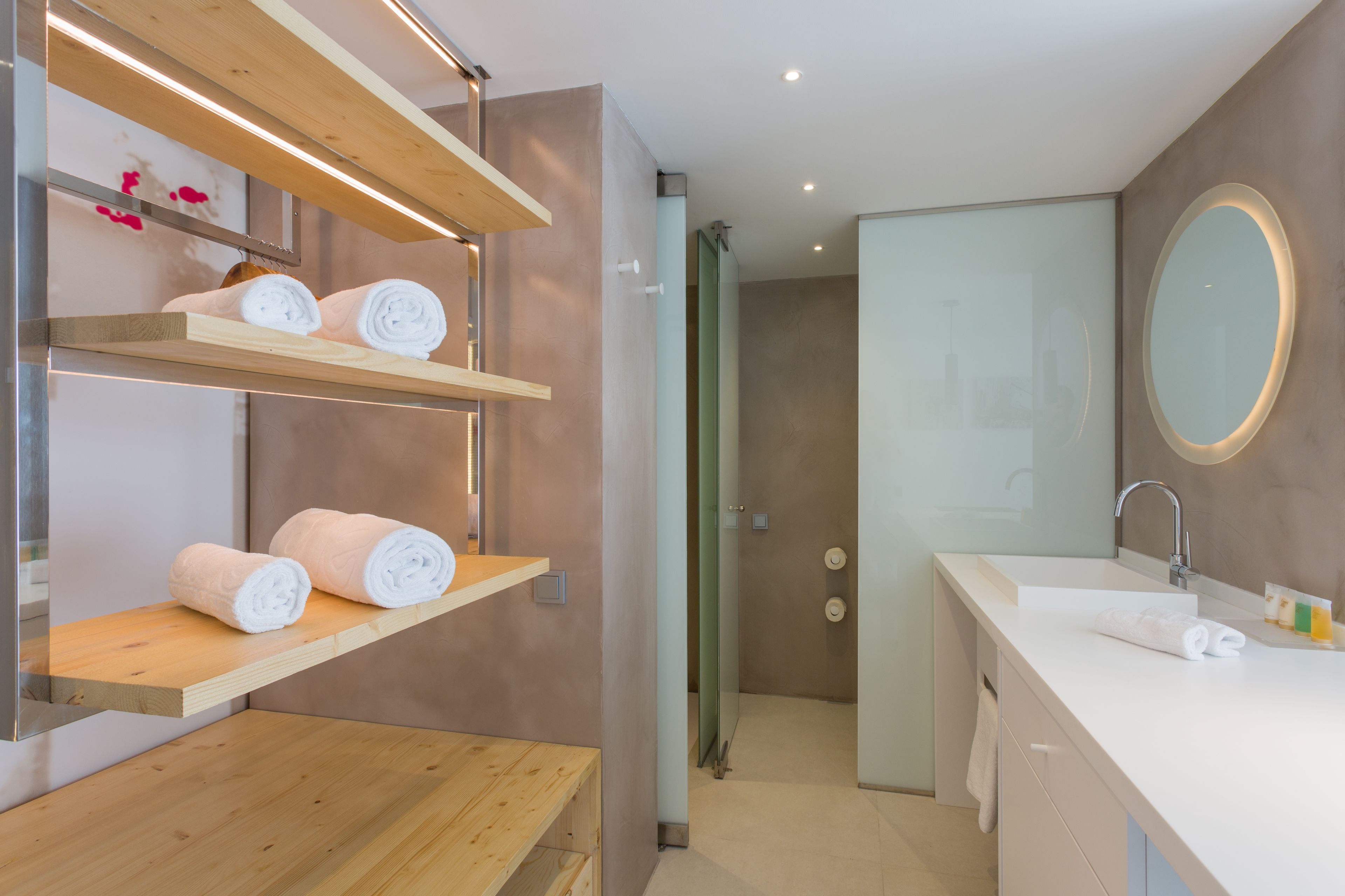 Une salle de bain moderne avec des étagères en bois où sont rangées les serviettes, un grand miroir et un espace douche.