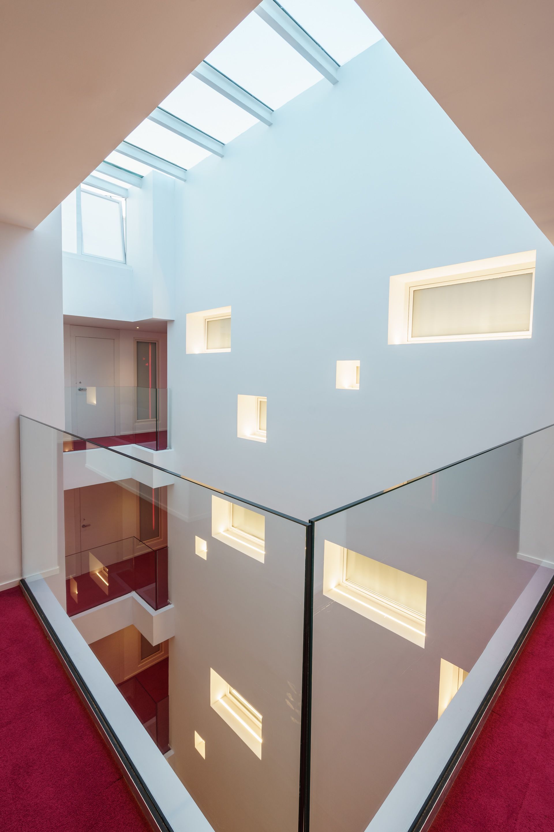 Un interno moderno con ringhiera in vetro, tappeto rosso e lucernario.